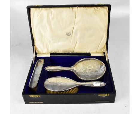 A cased George V hallmarked silver four-piece dressing table set comprising hand mirror, brush, a gentlemen's brush and silve