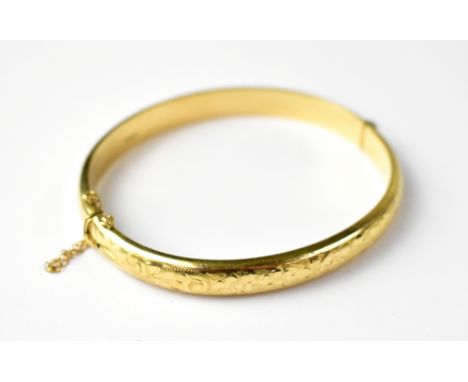 A 9ct gold hinged bracelet with floral chased pattern, with safety chain, approx 10.7g. CONDITION REPORT: The bangle is diffi