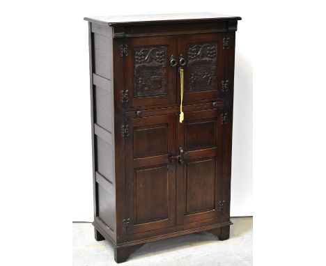 A reproduction oak cocktail cabinet, the upper section with two carved panel doors decorated with interior scenes, partially 