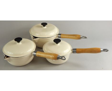 Three Le Creuset style cream enamel pans, each with turned wooden handles
