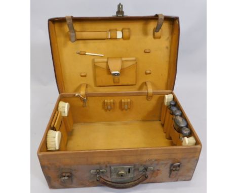 An early 20thC leather dressing case, bearing the initials HNDM, containing a number of ivory brushes, glass jars with silver