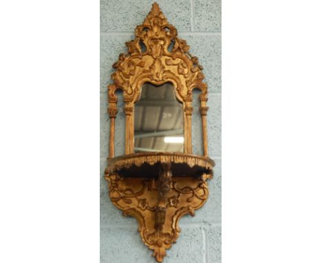 A Continental gilt wood and gesso wall bracket, the later mirror plate surrounded by leaf craft frame, etc., with a bow front