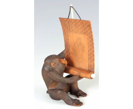A JAPANESE MEIJI PERIOD CARVED BOXWOOD AND IVORY OKIMONO finely modeled as a monkey with glass eyes holding a scroll with eng