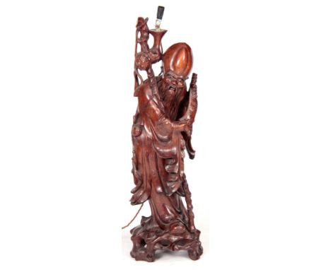 A 20TH CENTURY CHINESE CARVED HARDWOOD TABLE LAMP OF A STANDING BUDHA with ivory and ebony eyes, holding a scroll; on a natur