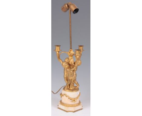 AN EARLY 20TH CENTURY FRENCH GILT ORMOLU AND WHITE MARBLE TABLE LAMP with putti holding a three branch candelabra, standing o