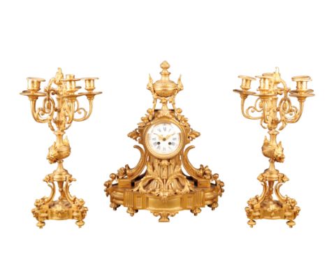 A LOUIS XV STYLE GILT METAL GARNITURE DU CHEMINEE, the clock with a convex enamelled dial and blue Arabic and Roman numerals,