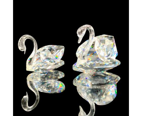 A pair of clear crystal swans that are at rest with their heads faced downwards. Swarovski backstamp. Dimensions of the large