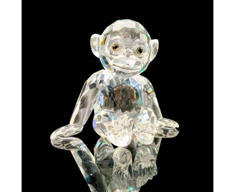 A clear crystal figure depicting a young chimpanzee that is sitting on his bottom with his arms outstretched. Swarovski backs