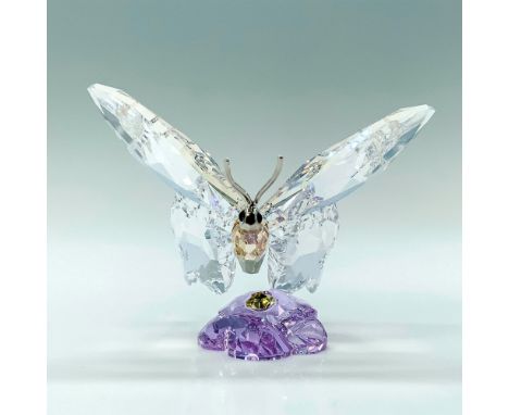 A clear crystal butterfly with a rhodium face and antennas that is sitting on a purple crystal flower. Swarovski backstamp. T