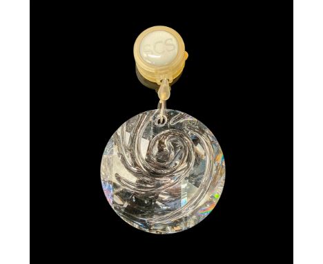 A clear round crystal ornament with carvings that resemble wind carved into the center. Swarovski backstamp. This item has it