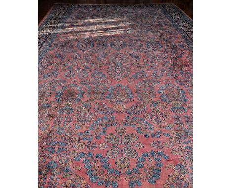 A Sarouk carpet, the pink field decorated overall with a design of flowering branches in tones of blue and ochre, within navy