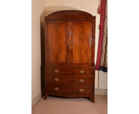 A George III mahogany clothes press, circa 1810, the arched cornice above a pair of ebonised strung doors, opening to a hangi