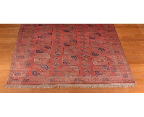 A Bokhara carpet, the madder field decorated with rows of guls and stylised lozenge motifs in tones of navy and cream, 417 x 