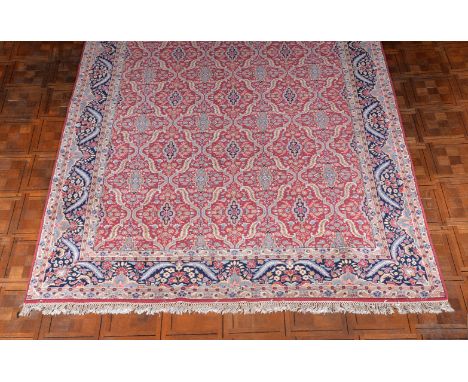 A Kirman carpet, the crimson field decorated with an overall design of tessellating medallions formed of stylised leaves, dec