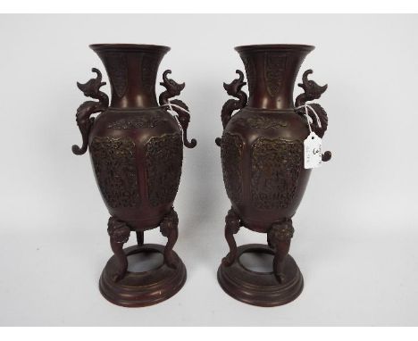 A pair of cast metal vases with twin chilong handles, cast decorative panels, raised on tripod mask and tongue supports risin