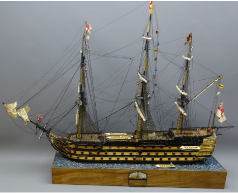 Wooden solid hull scale model of HMS Victory, furl rigged flying signal flags, with lifeboat on stand with ocean textured top