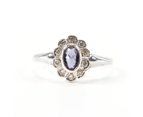 A hallmarked 9ct white gold iolite and diamond cluster ring. The ring set with a central oval cut iolite framed by a halo of 