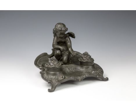 A patinated spelter seated cherub inkstand1920s, the cherub in a crouched pose, seated upon the shaped base, amidst a floral 
