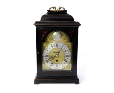 An ebony bracket clock, early 18th century, the caddy top with gilt metal foliate cast swing handle above an arched glazed do