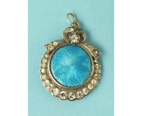 An Edwardian silver circular pendant, with blue guilloche enamel plaque within graduated paste-set surround, hair locket to r