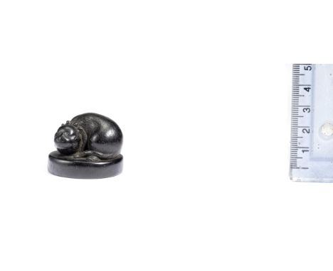 An ebony netsuke of a catBy Futsuhira, 18th centuryLying asleep on an oval base, its body curled to the left and a knotted co