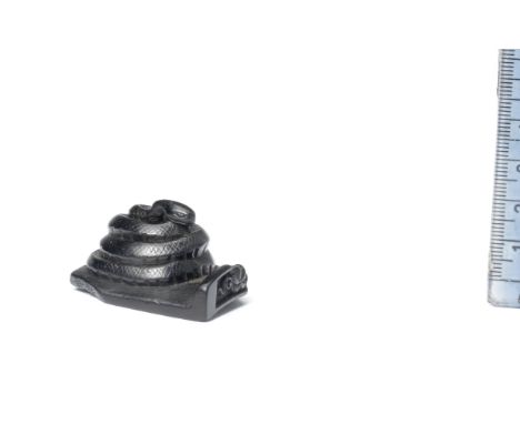 An ebony netsuke of a snake19th centuryThe slender reptile tightly coiled on a discarded broken roof tile, the end of which i