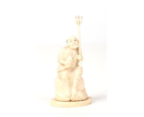 A Japanese Meiji period carved ivory okimono. Formed as a fisherman seated upon a rock, holding a trident in one hand and a f