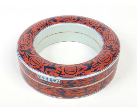 A 20th century Chinese ring formed box and cover. Ground in rouge de fer enamel and painted in underglaze blue with cranes, c