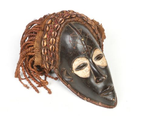 A West African Ivory Coast hardwood tribal mask. With cloth and rope work coiffure adorned with beadwork and cowrie shells, t