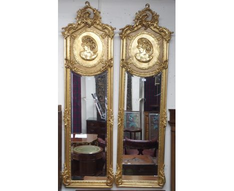 A pair of 20th century gilt Rococo style peer mirrors with scrolled foliate surmount over oval portrait over shaped bevelled 