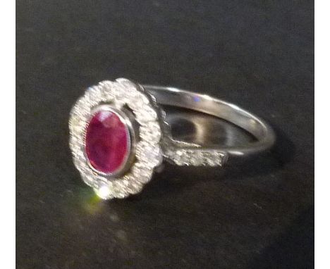 An 18ct White Gold Ruby and Diamond Ring, with a central oval Ruby surrounded by diamonds within a pierced setting.