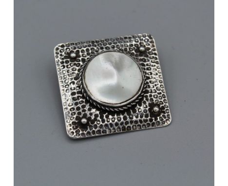 An Arts and Crafts brooch in a square shape and set with a mabe pearl/mother of pearl, bezel set with twisted wire surround o