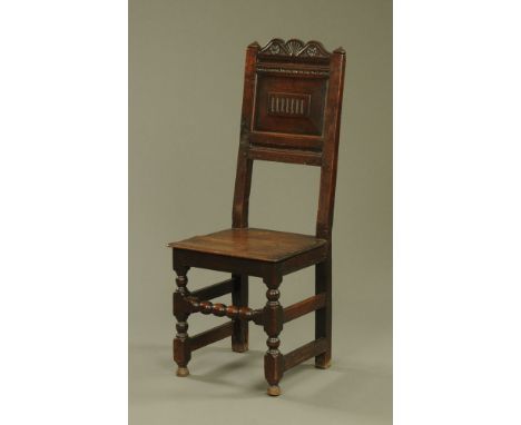 A 17th century oak chair, with carved cresting rail and single panelled back with solid seat and turned legs with bobbin fron