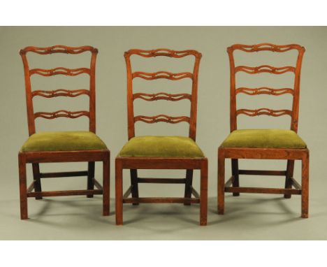 A set of three George III elm ladder back dining chairs, with pierced shaped splats, the drop in seats upholstered in green c