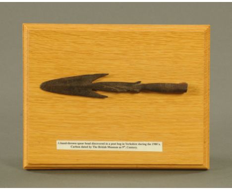 A barbed metal spear or arrowhead, mounted on an oak plaque and marked "A hand thrown spearhead discovered in a peat bog in Y
