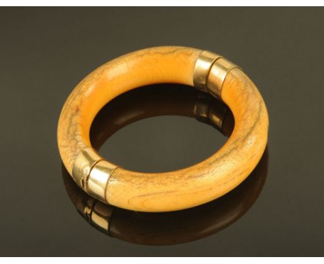 An antique ivory bangle, with yellow coloured metal mounts. CONDITION REPORT: The measurements are 8.3 cm and 9 cm.  The bang