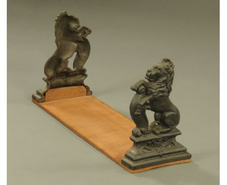 A Victorian and later book trough formed from a pair of cast iron rampant lion door porters mounted on a plywood base, 40 cm 
