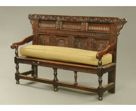 An antique oak settle, with carved panelled back silhouette arms and solid seat with turned legs and stretchers and complete 