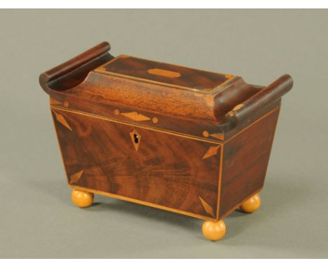 A George IV figured mahogany sarcophagus shaped tea caddy, the lid with scrolled ends, on ball feet.  13.5 cm high.
