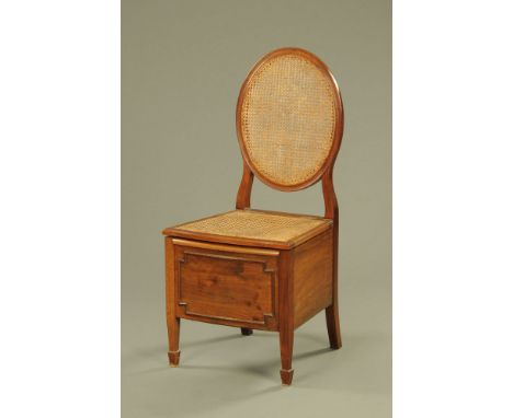 An Edwardian mahogany commode chair of Sheraton style, with caned back and seat raised on square tapered front legs.  106 cm 