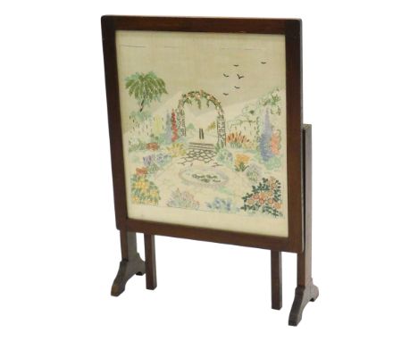 A 1920s oak fire screen table, inset with a needlework banner of a cottage garden, 49cm wide. 