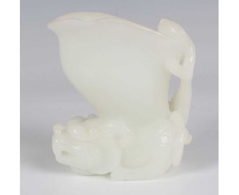 A Chinese pale celadon jade libation cup, 20th century, the horn shaped bowl supported by a crouching Buddhistic lion, carved