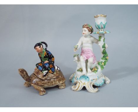 A candlestick in the 18th century Chelsea manner with applied figure of a cherub and floral garland, with gilt anchor mark to
