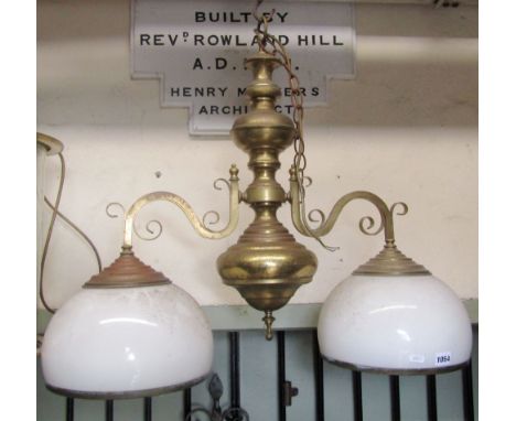 A hollow brass two branch hanging ceiling light with knopped stem supporting two scrollwork branches with domed opaque glass 