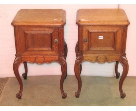 A pair of medium to light oak bedside cupboards enclosed by moulded panelled doors with shaped aprons and scrolled cabriole s