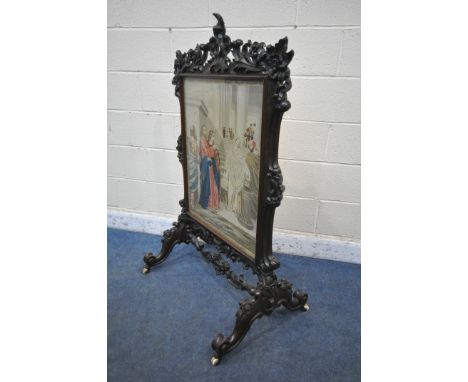 A VICTORIAN WALNUT FIRE SCREEN, the heavily carved frame with scrolling and foliage, on shaped legs and ceramic castors, the 