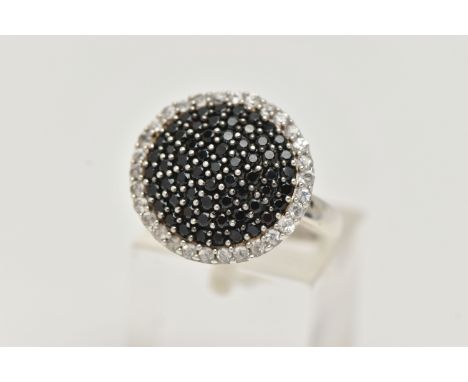 A GEM SET CLUSTER RING, comprised of black circular cut stones, pave set with a surround of colourless topaz, set in a white 