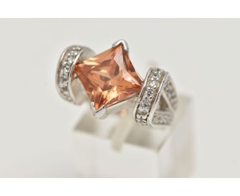 A WHITE METAL DRESS RING, principally set with a large square cut orange cubic zirconia, leading on to a looped design should