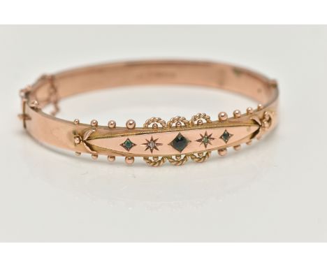 A 9CT GOLD EDWARDIAN BANGLE, rose gold hinged bangle, set with three green stones assessed as two small emeralds and a centra