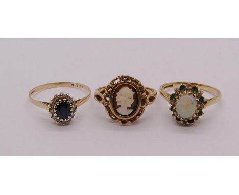 Three 9ct dress rings comprising a sapphire and diamond cluster, an opal, emerald and diamond cluster and a cameo example, 6.